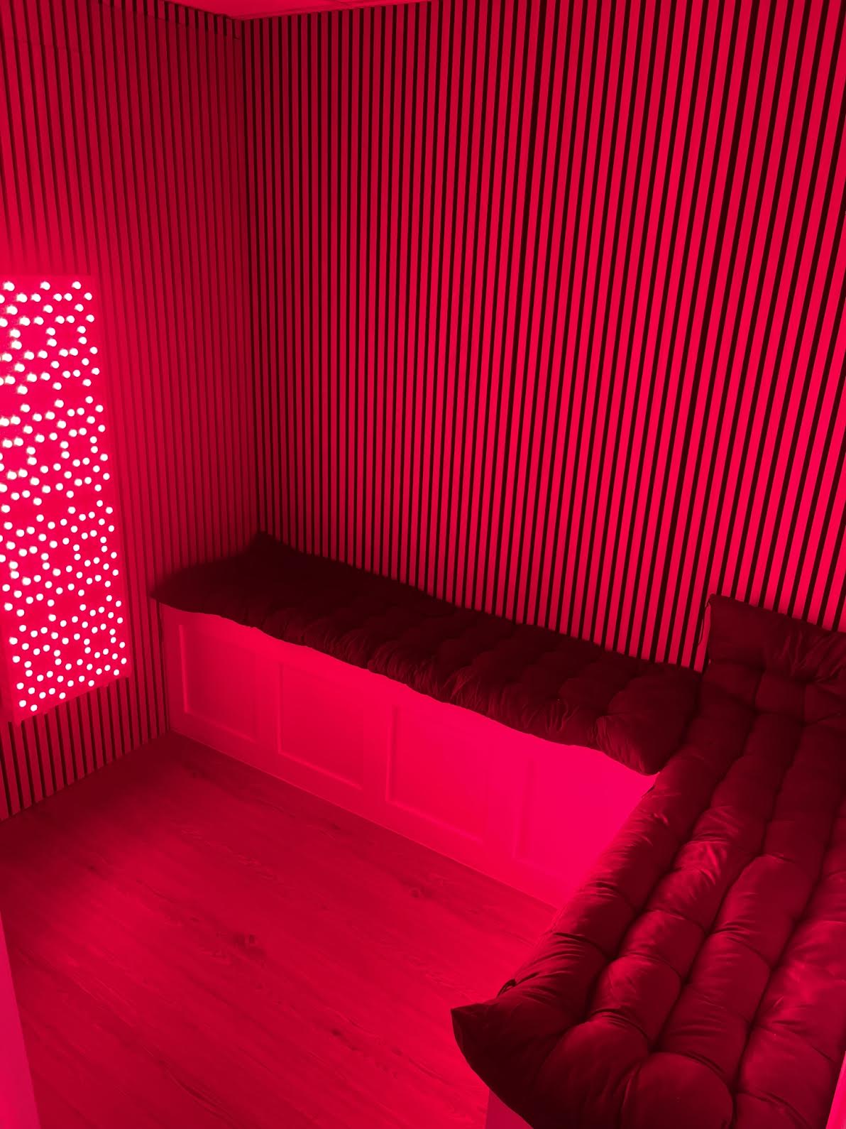 Pure Core red light therapy room with slatted walls, cushioned bench seating and a full-length red light panel
