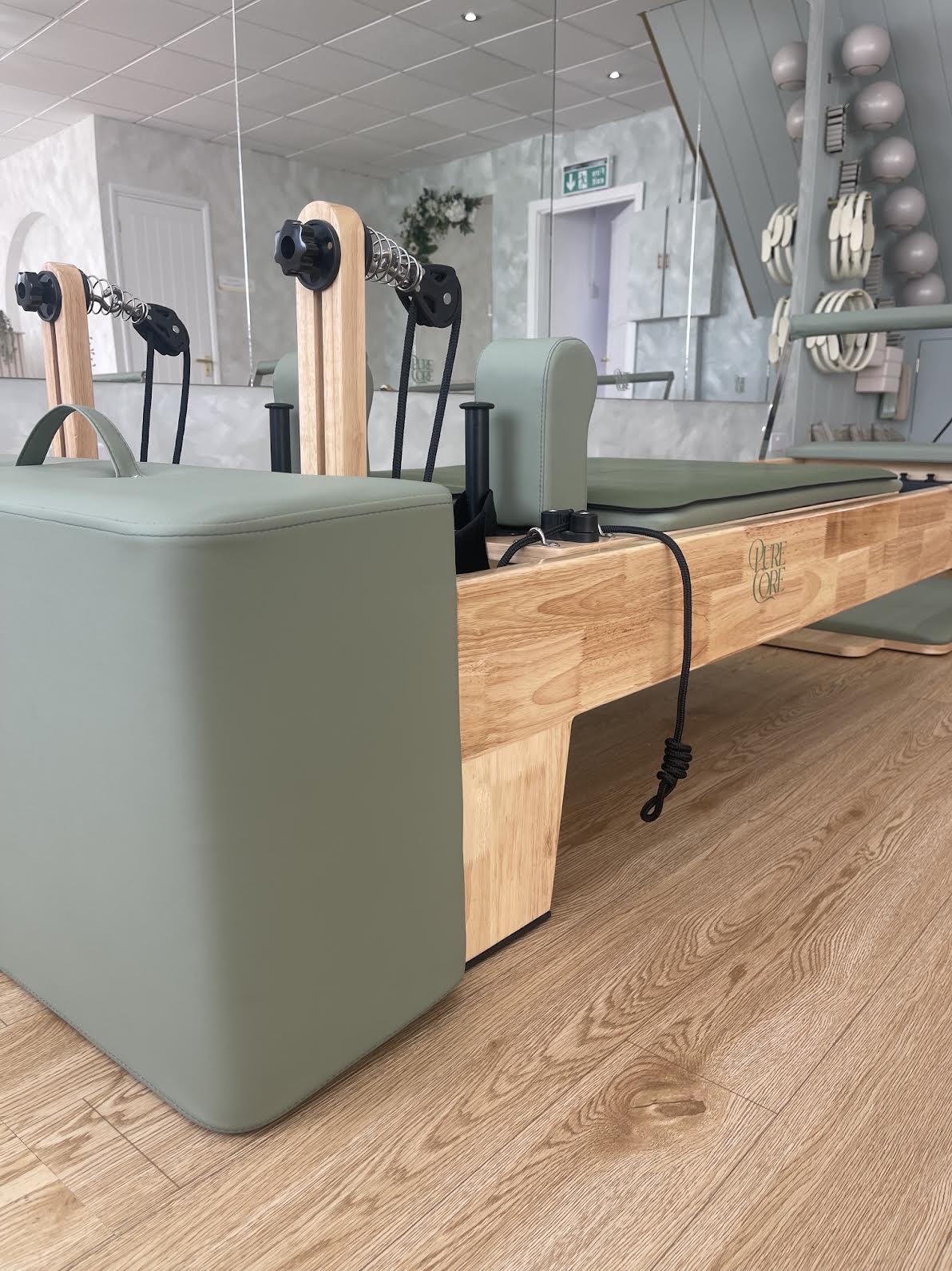 Close view of a sage-upholstered reformer with the Pure Core mark on the frame